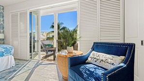Quarto com cama, sofá azul, mesa de madeira redonda e vista para a varanda.