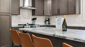 A modern kitchen with dark cabinets, a marble countertop, and a bottle of champagne. - Off Leash Oasis - Brand New Hot Tub & Fire Pit - Pet Friendly! (Indianapolis)