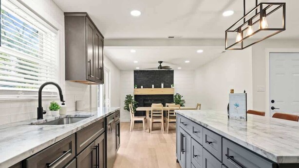 A modern kitchen with a central island, dark cabinetry, and a dining area with wooden chairs. - Off Leash Oasis - Brand New Hot Tub & Fire Pit - Pet Friendly! (Indianapolis)