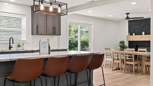 A modern kitchen with a bar area, wooden cabinets, and a dining table with chairs. - Off Leash Oasis - Brand New Hot Tub & Fire Pit - Pet Friendly! (Indianapolis)