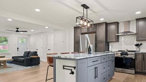 A modern kitchen with grey cabinets, a central island, stainless steel appliances, and a pendant light fixture. - Off Leash Oasis - Brand New Hot Tub & Fire Pit - Pet Friendly! (Indianapolis)