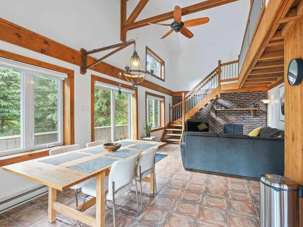 A spacious living area with a wooden staircase, a dining table with chairs, and a sofa.
