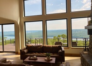 Ein geräumiges Wohnzimmer mit großen Fenstern und einem herrlichen Blick auf einen See und Berge.
