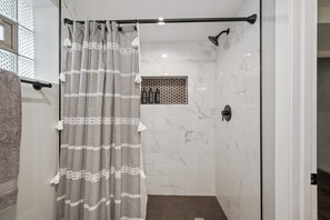 A shower area with a glass door, a towel rack, and a showerhead. - Unique Home in Maywood - 5 Bedroom (Maywood)