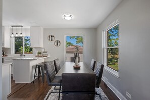 A modern kitchen with a dining area, featuring a large island, dark chairs, and pendant lighting. - Unique Home in Maywood - 5 Bedroom (Maywood)