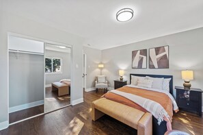 A bedroom with a large bed, a closet with sliding doors, a chair, and two bedside lamps. - Unique Home in Maywood - 5 Bedroom (Maywood)