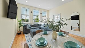 Uma sala de estar moderna com um sofá seccional, uma mesa de jantar com pratos e copos verdes, e um espelho grande na parede.