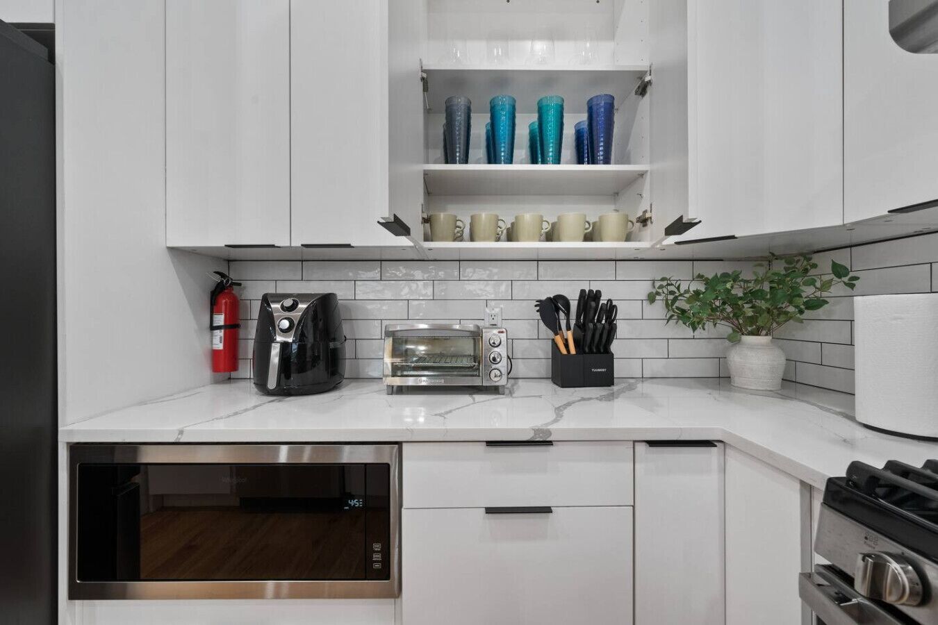 Una cocina moderna con gabinetes blancos, horno empotrado, tostadora, cafetera y una planta.