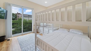 Quarto com beliche, porta de vidro corria para uma varanda, e vista para áreas verdes e edifícios.