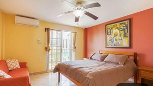 A bedroom with a bed, a ceiling fan, a window, and a painting on the wall. - Paradise Suites & Residence  (San Pedro)