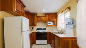 A compact kitchen with wooden cabinets, a white refrigerator, a stove, a microwave, and a water dispenser. - Paradise Suites & Residence  (San Pedro)