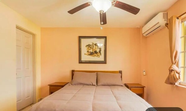 A bedroom with a bed, a ceiling fan, an air conditioning unit, a framed picture on the wall, and a window with curtains. - Paradise Suites & Residence (San Pedro)