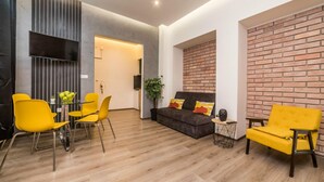 Una sala de estar moderna con un sofá, dos sillones amarillos, una mesa de centro y un televisor montado en la pared.