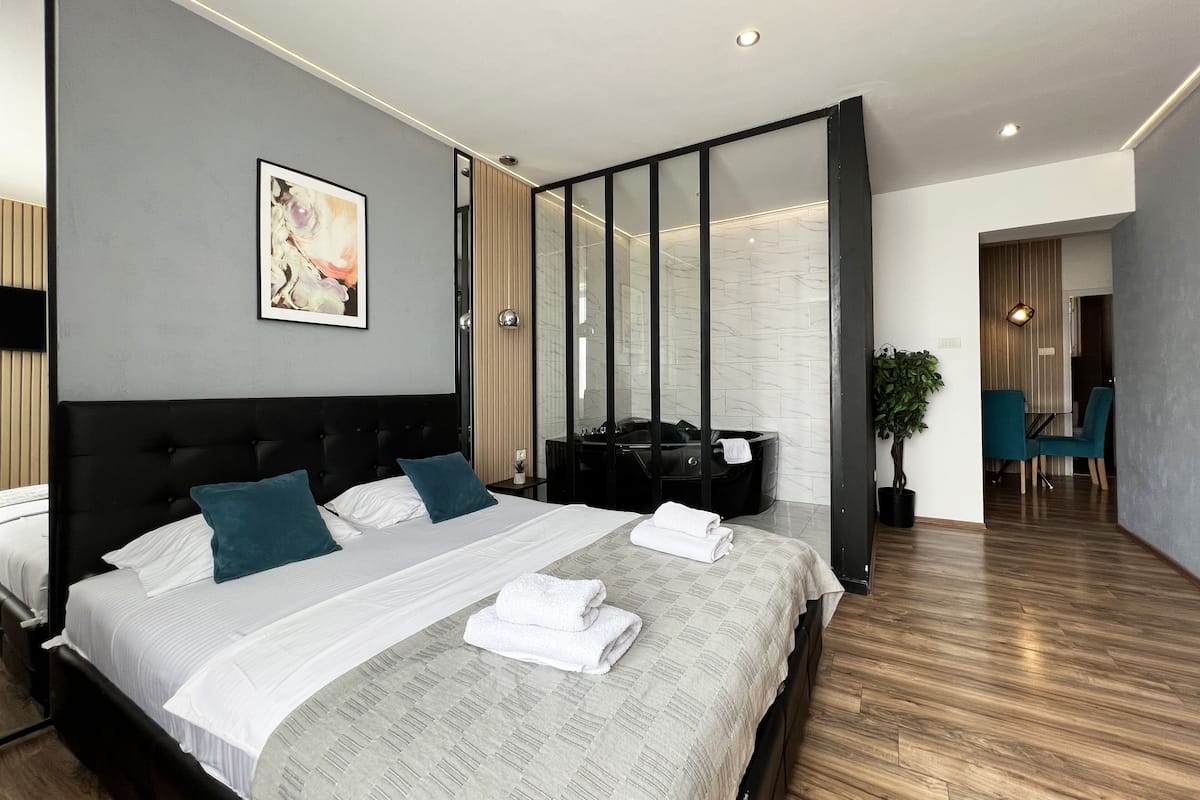 A modern hotel room with a large bed, a seating area with chairs, and a view of the hallway.