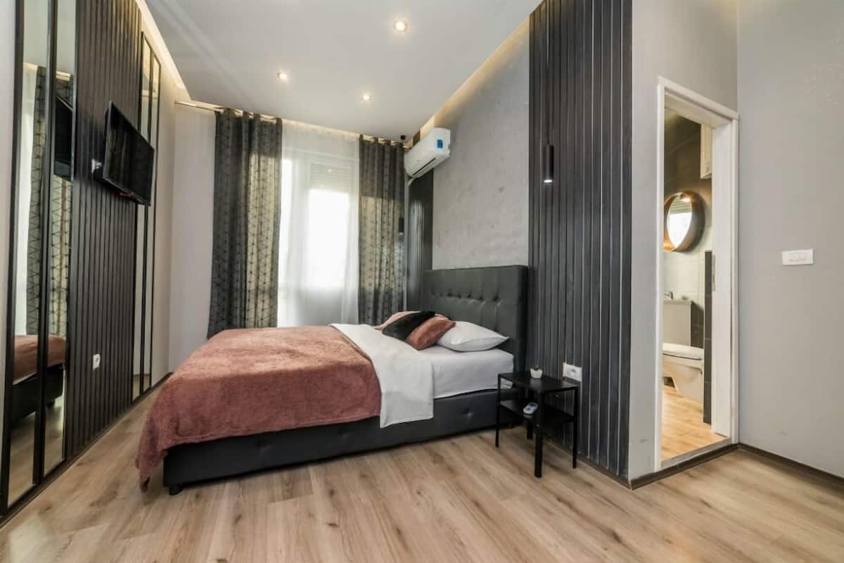 A modern bedroom with a large bed, a TV mounted on the wall, and a mirror in the corner.
