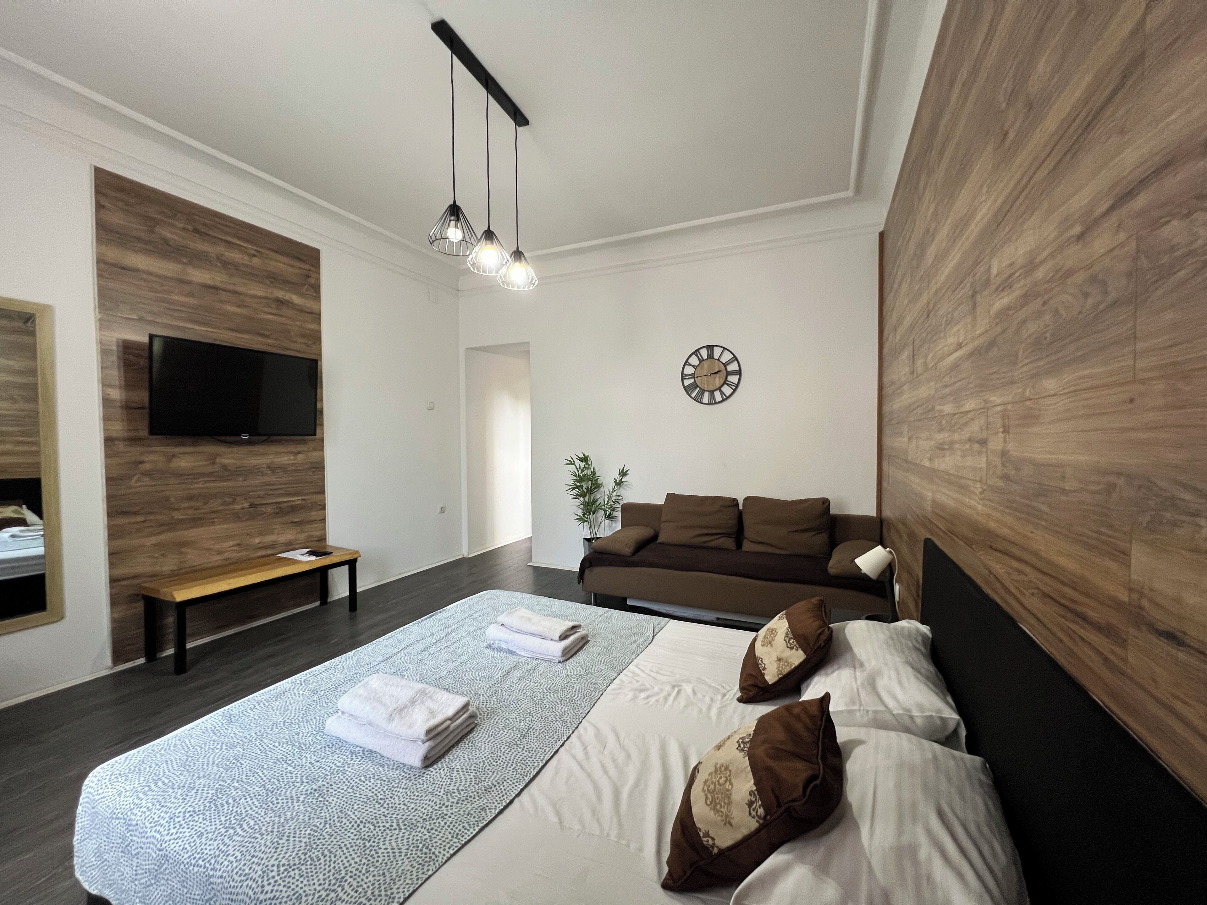 Ein modernes Hotelzimmer mit einem großen Bett, einer Wandpaneele aus Holz, einem Flachbildfernseher, einem Nachttisch und einer Bank.