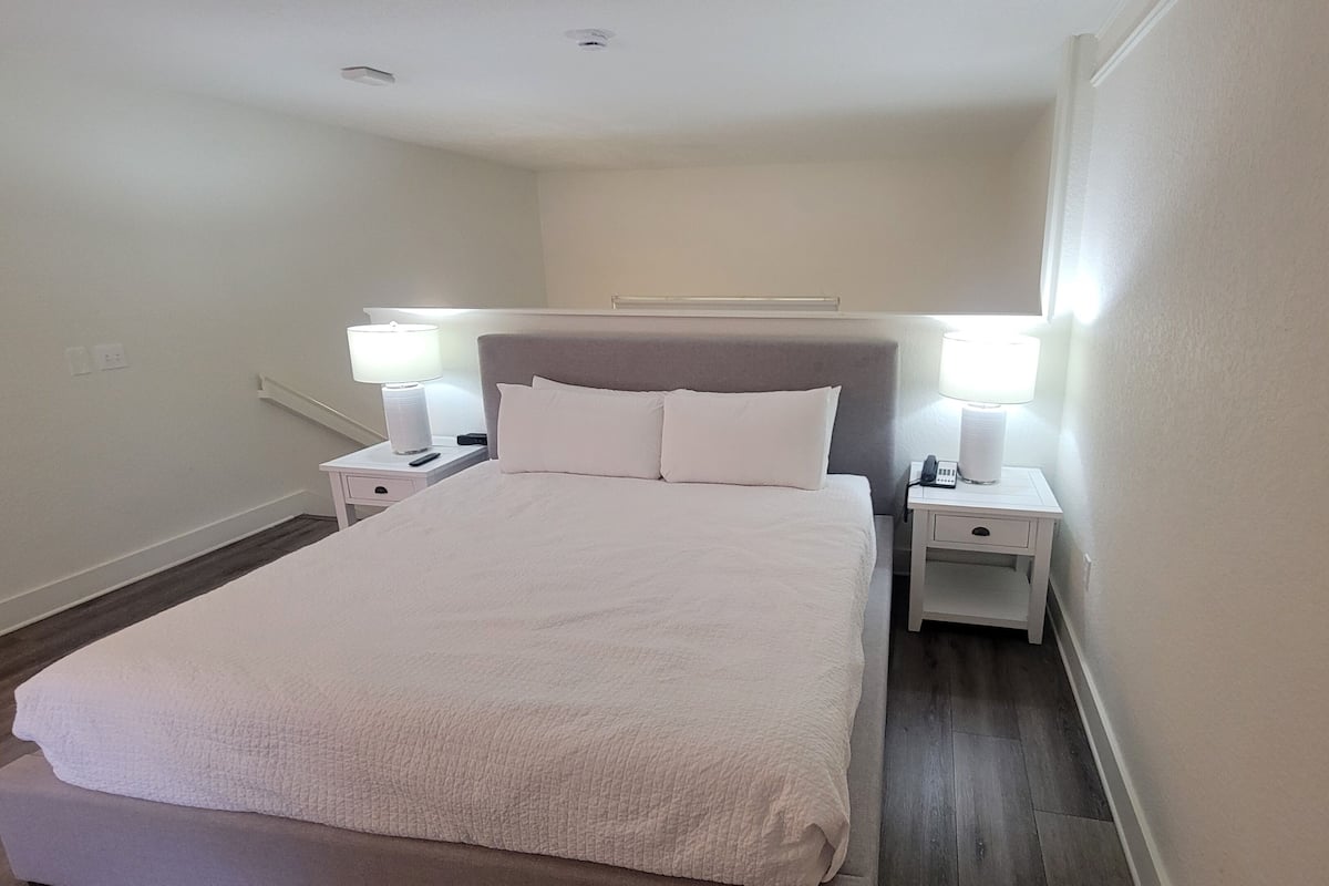 Una cama bien tendida con sábanas blancas, dos mesitas de noche con lámparas y un cabecero.