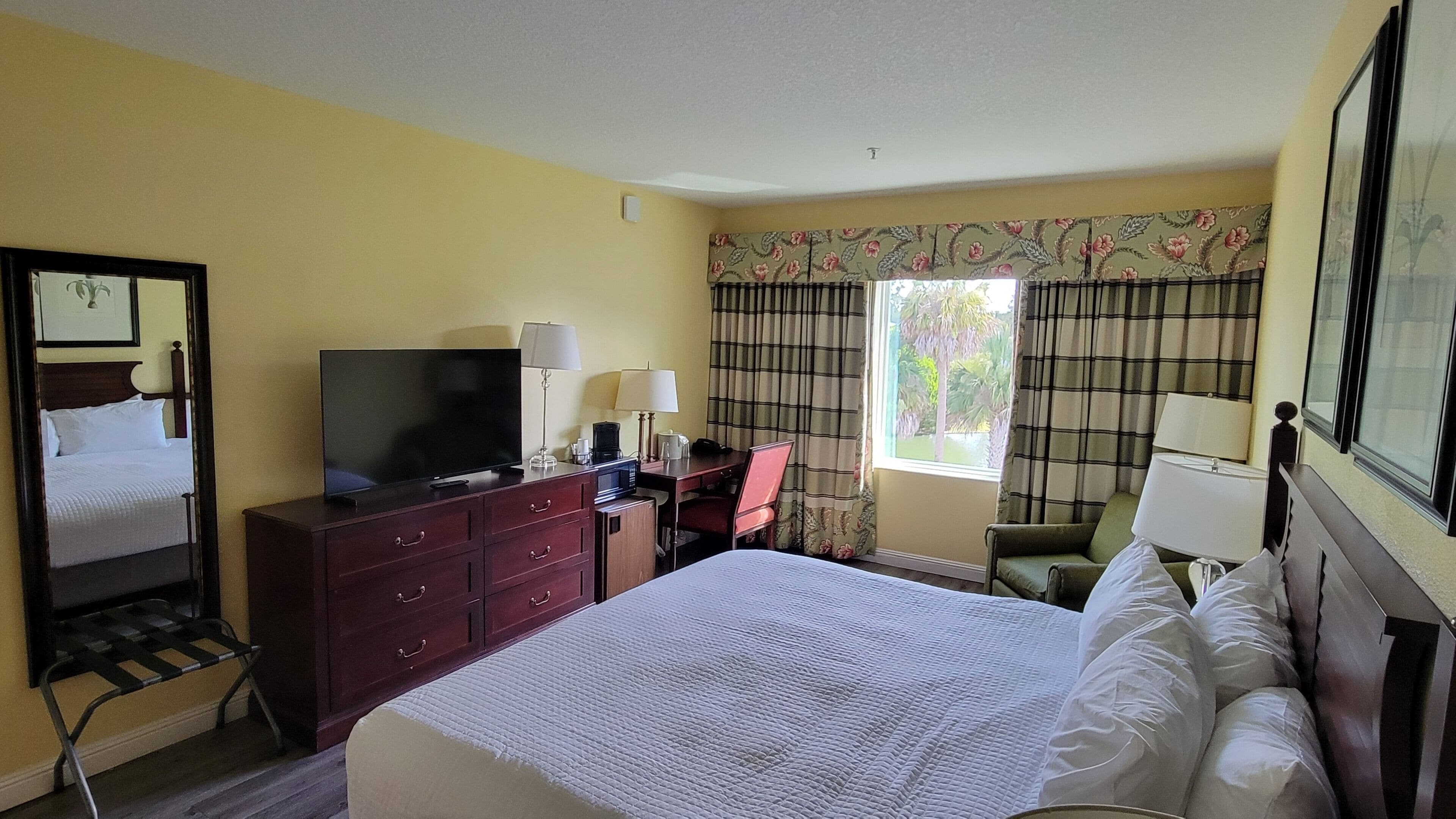 Una habitación de hotel con cama, escritorio, televisor y ventana con cortinas.