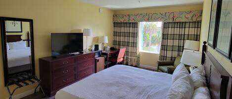 A hotel room with a bed, a desk, a television, and a window with curtains.