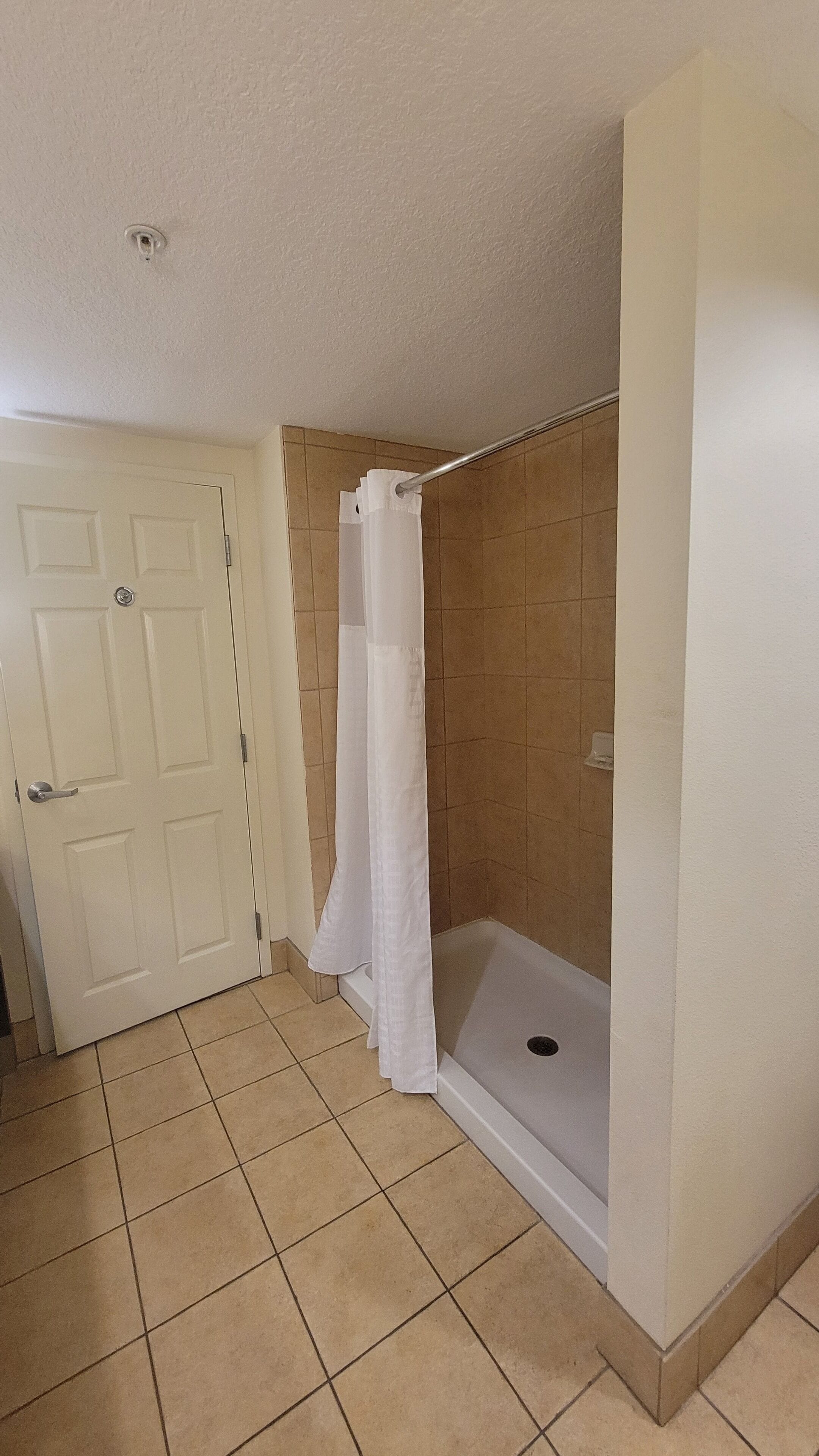 Un baño con ducha, una puerta y suelo de baldosas.