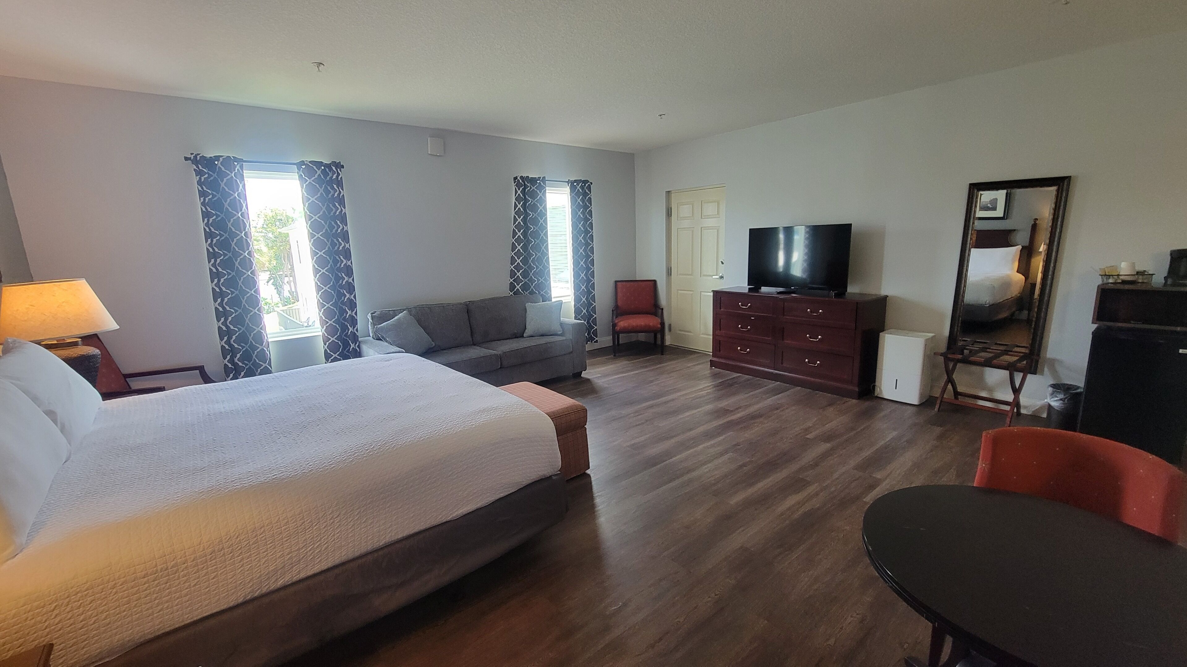 A hotel room with a bed, a sofa, a TV, a dresser, and a desk.