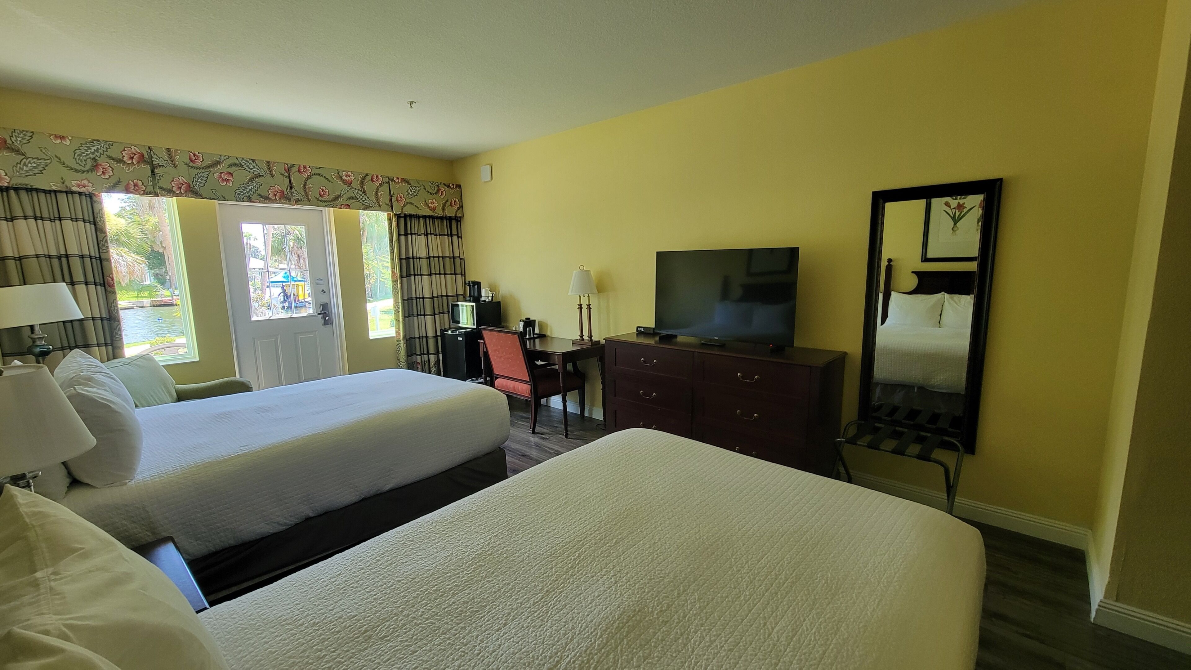 Una habitación de hotel con dos camas, televisor, cómoda y espejo.