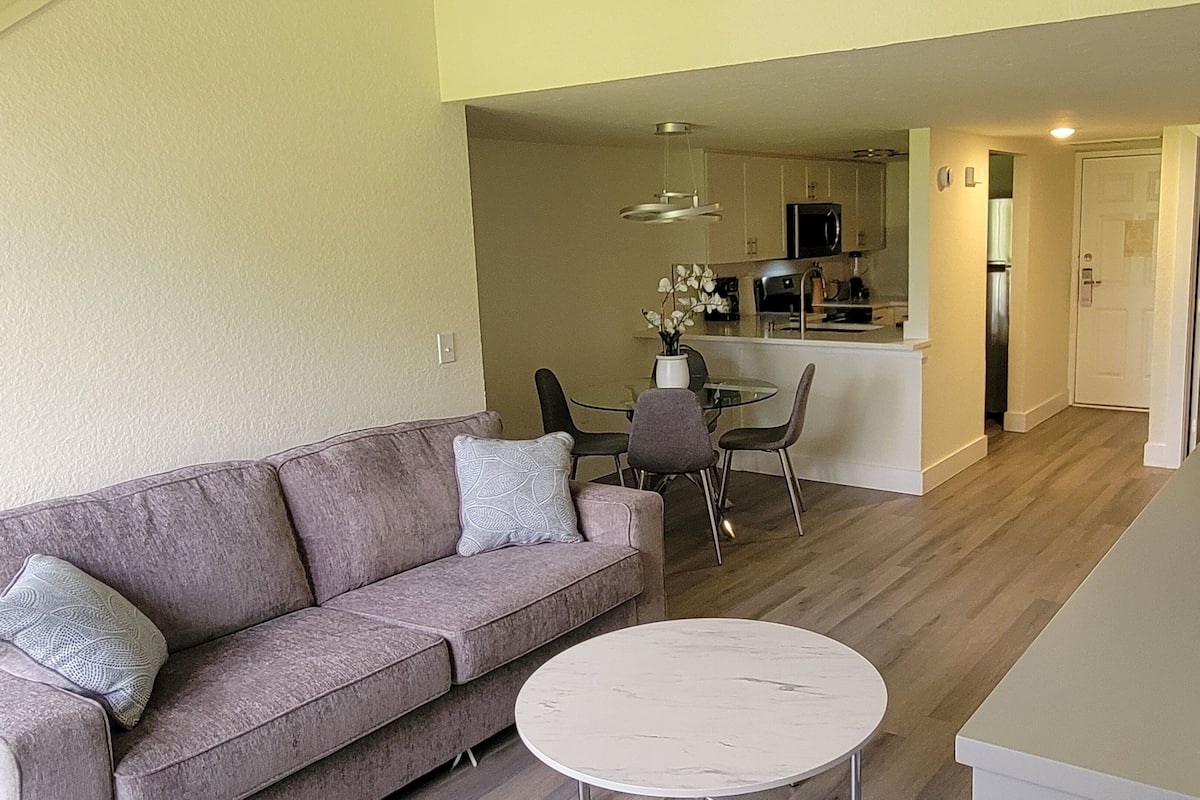 Una sala de estar moderna con un sofá, una mesa redonda de centro y un comedor con sillas y una pequeña mesa.
