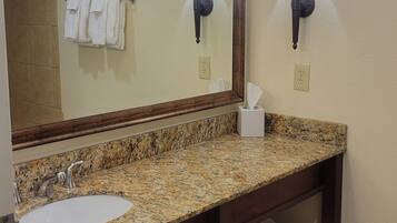 A bathroom with a large mirror, granite countertop, sink, towel rack, two wall-mounted lights, and a trash can.