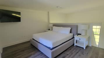 A hotel room with a bed, a nightstand, a TV mounted on the wall, and a window with a view.
