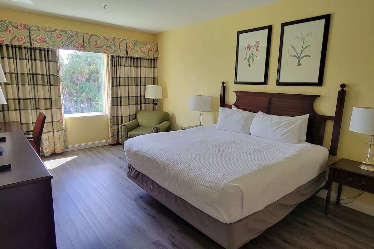 Habitación de hotel con una cama grande, dos lámparas de noche, un escritorio con lámpara, una silla y una ventana con cortinas.
