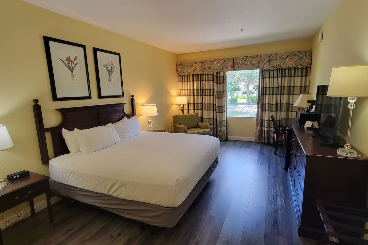 Habitación de hotel con una cama grande, un escritorio, una silla, un aparador y dos láminas botánicas enmarcadas en la pared.