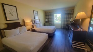 Habitación de hotel con dos camas, un escritorio, una silla, una lámpara y una ventana con cortinas.