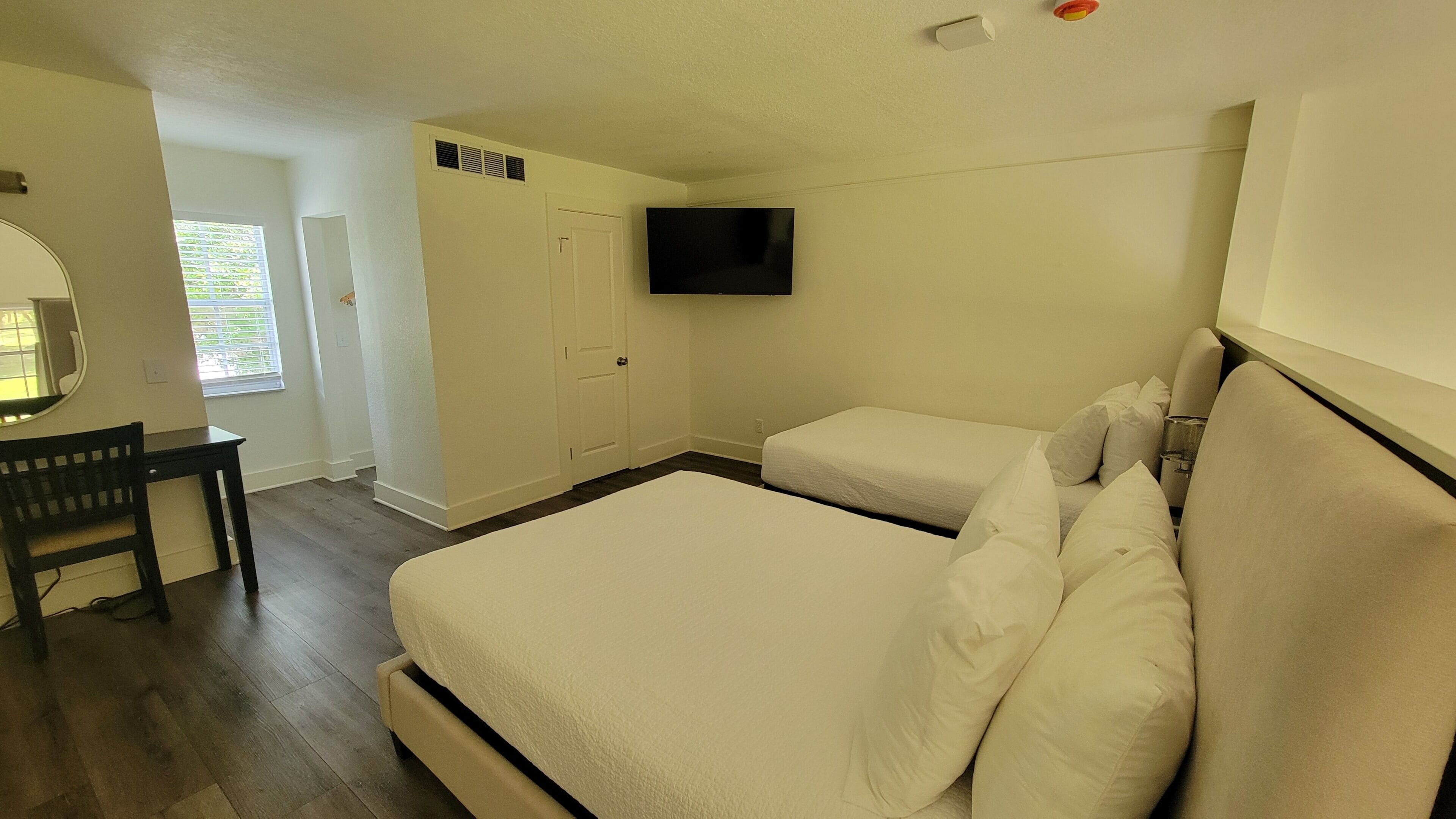 A bedroom with two beds, a TV, a desk, and a window.