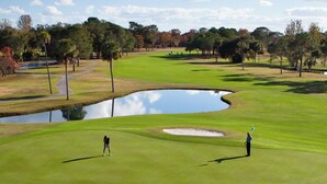 Un campo de golf con un estanque, árboles y un cielo despejado.