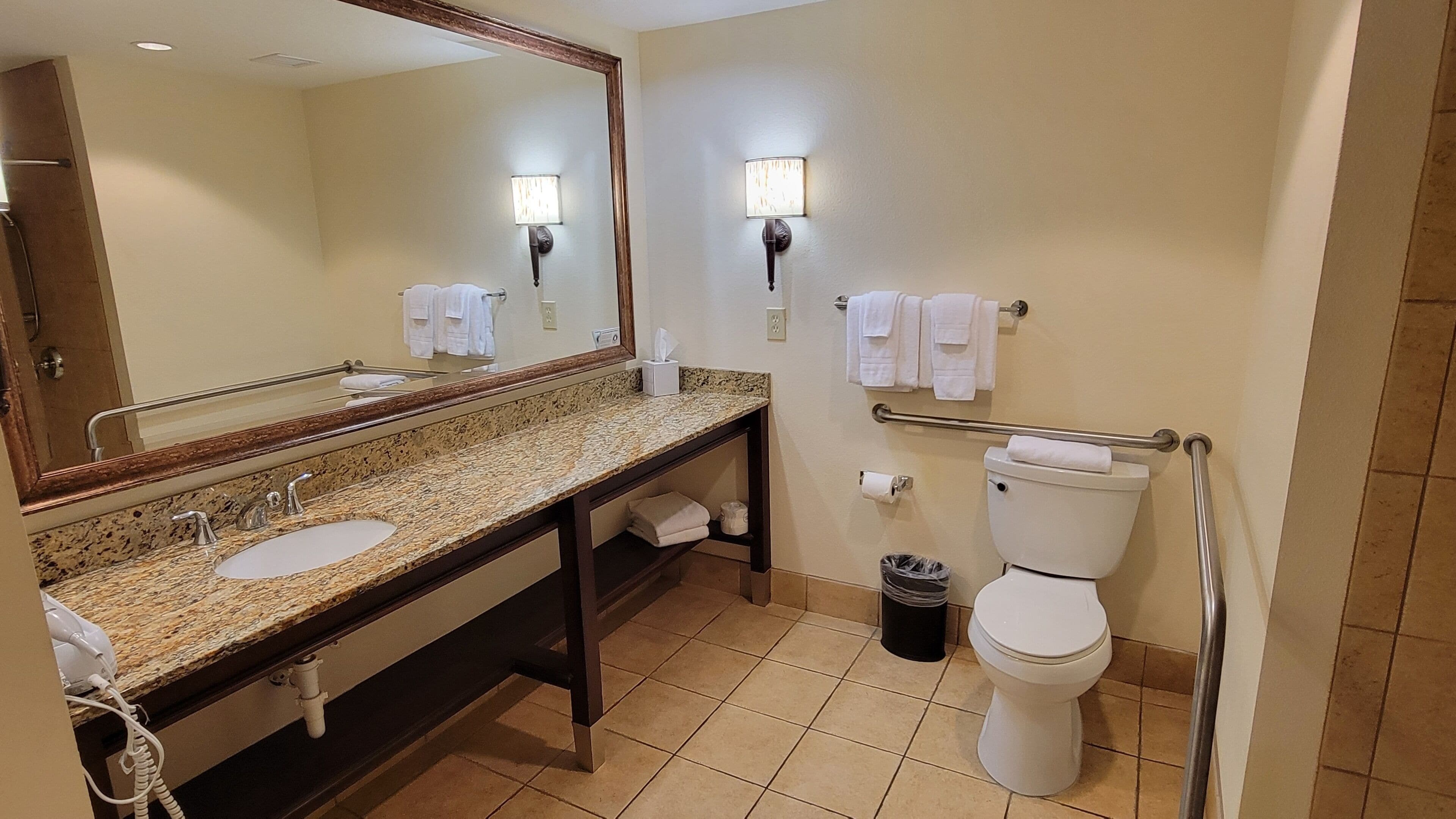 A bathroom with a sink, mirror, towel rack, toilet, and trash can.