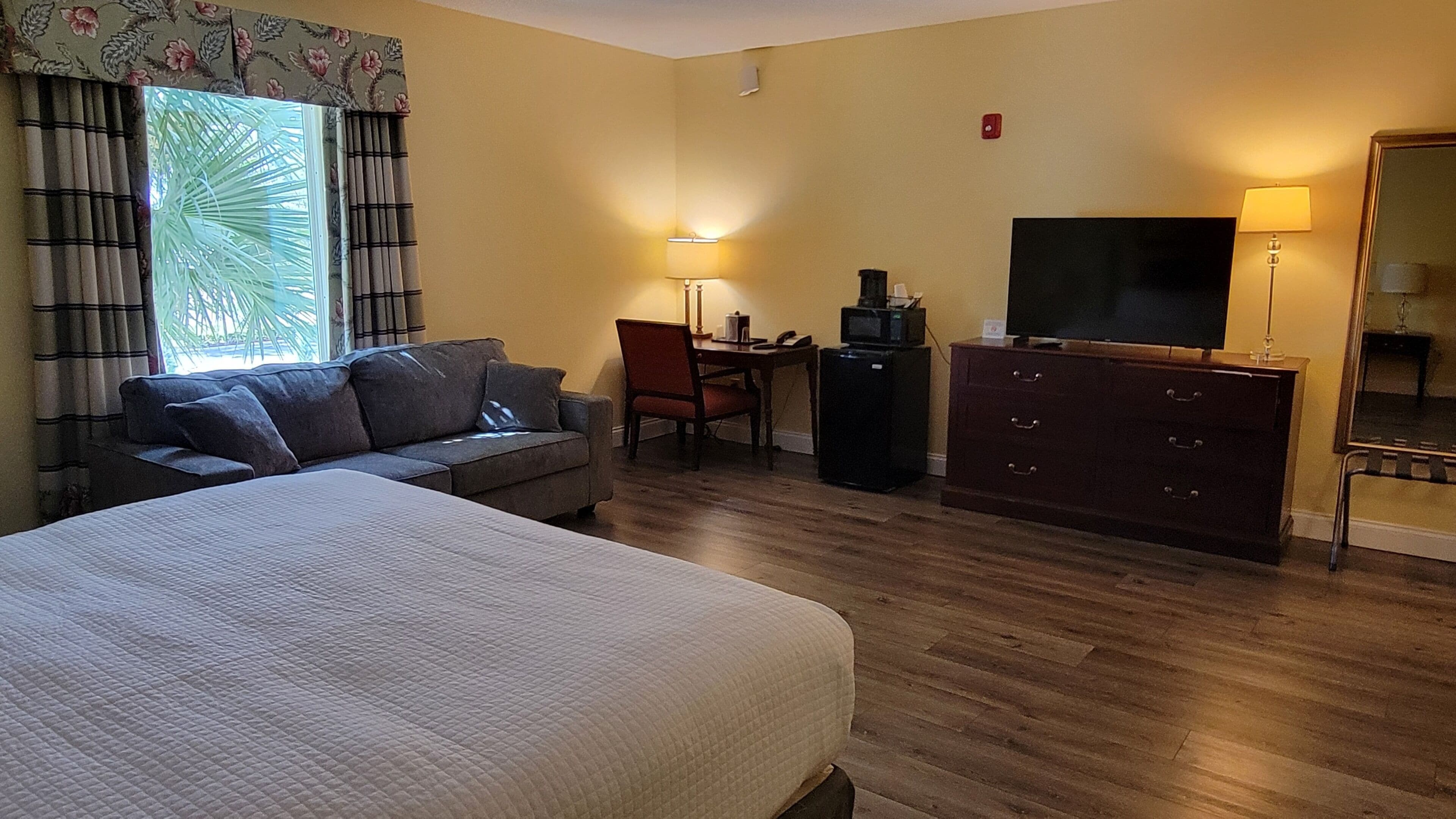 A hotel room with a bed, a sofa, a desk with a chair, a television, and a dresser.