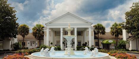 A grand building with a central fountain surrounded by colorful flower beds.