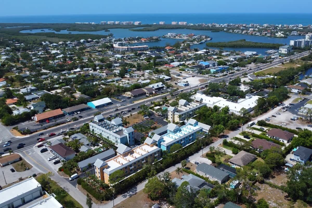 An aerial view of a coastal town with a mix of residential and commercial buildings, a main road, and a marina.