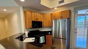 A modern kitchen with wooden cabinets, a stainless steel refrigerator, a black microwave, and a black countertop. - Breezy Escape – Free Parking – Bonita Beach (Bonita Springs)
