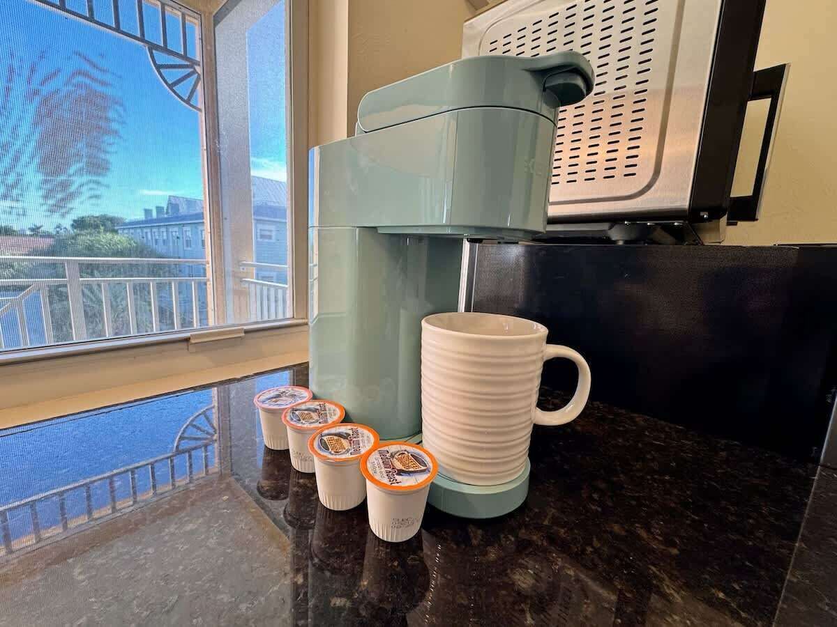 A coffee machine with a milk frother and a stack of disposable cups on a kitchen counter.