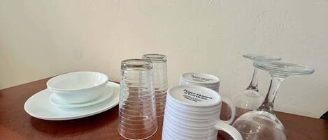A wooden table with white plates, clear glass mugs, and a clear glass decanter.