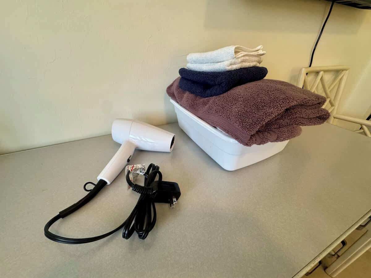 A hair dryer, a power cord, and a stack of towels on a countertop.