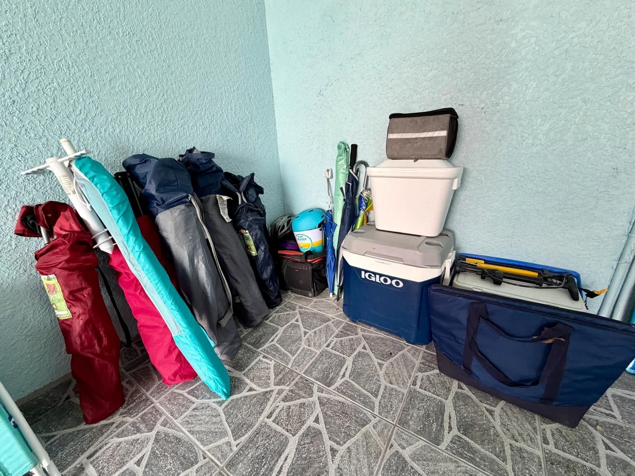 Un angolo con un mobiletto a parete che contiene diverse borse e un contenitore blu con l'etichetta 'IGLOO' su un pavimento piastrellato.