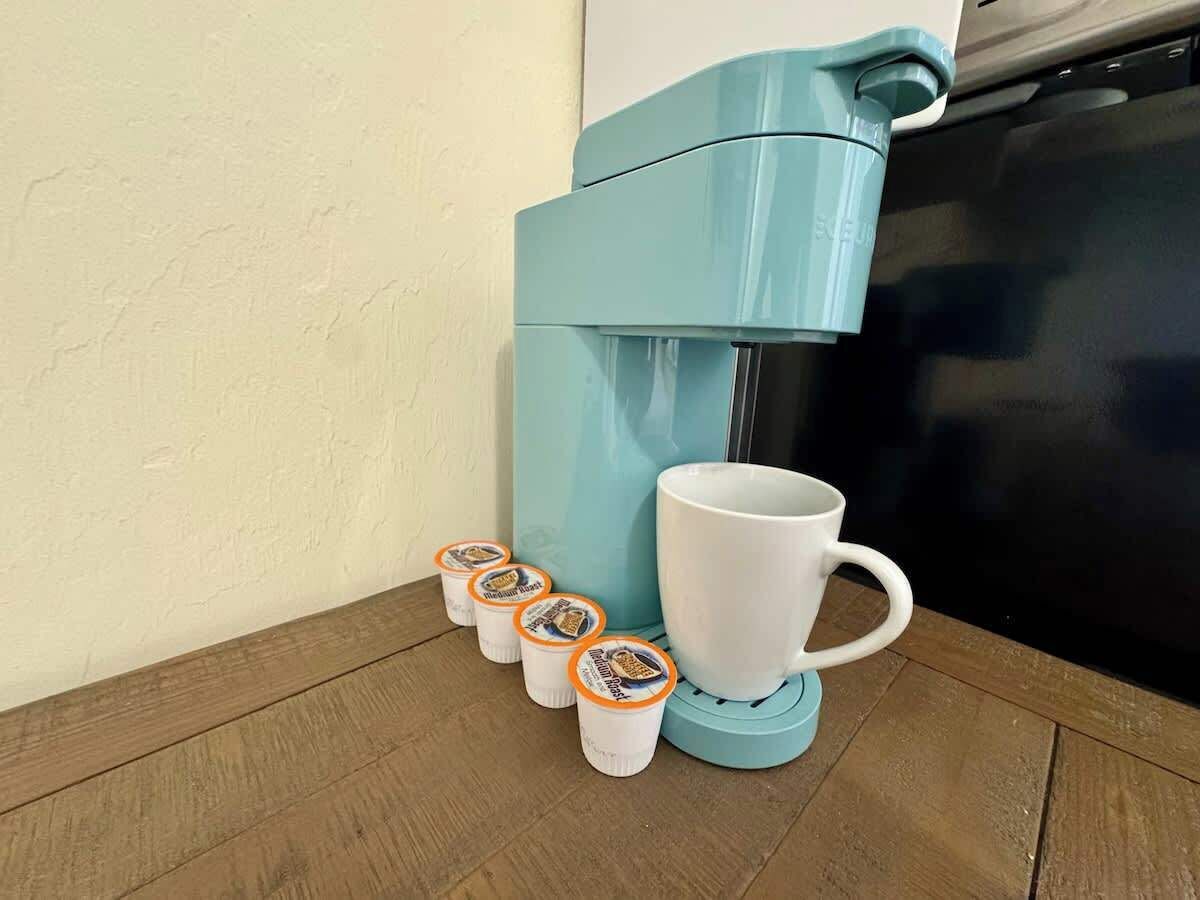 Una cafetera con cuatro tazas y una taza sobre un piso de madera.