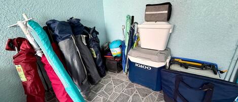 Rincón con un estante fijado a la pared que contiene varias bolsas y un enfriador azul con la etiqueta 'IGLOO' sobre un piso de baldosas.