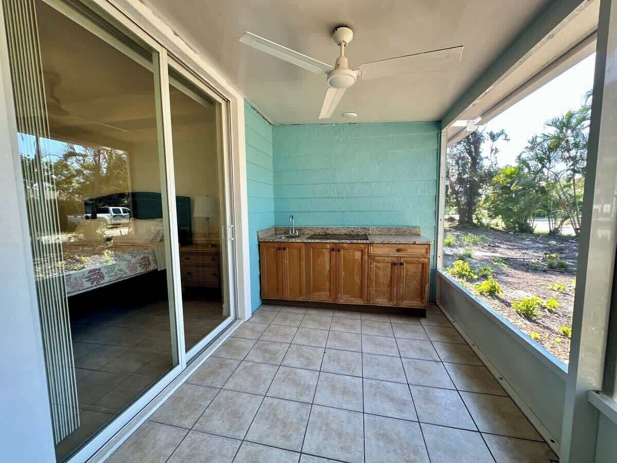 Ein Balkon mit einer Schiebetür, die zu einem Schlafzimmer führt, eine Küche mit Holdelementen und ein Deckenventilator.