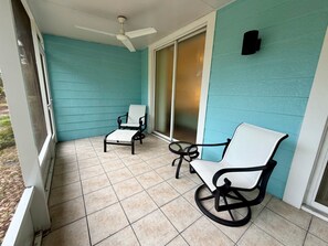 A covered patio with two chairs and a table, a ceiling fan, and a sliding glass door. - Modern Retreat – Beach Gear – Near the Sand (Bonita Springs)