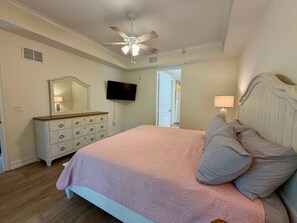 A bedroom with a bed, dresser, TV, ceiling fan, and a door leading to another room. - Modern Retreat – Beach Gear – Near the Sand (Bonita Springs)