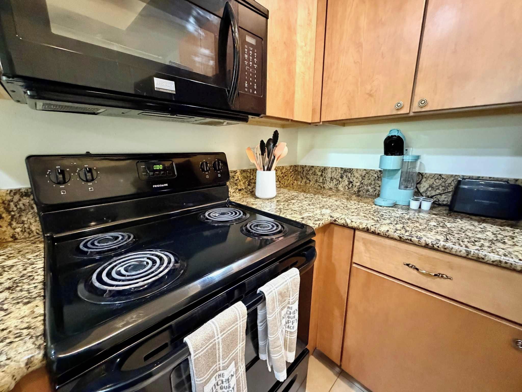 A kitchen with a black stove, a microwave above it, wooden cabinets, and a granite countertop.
