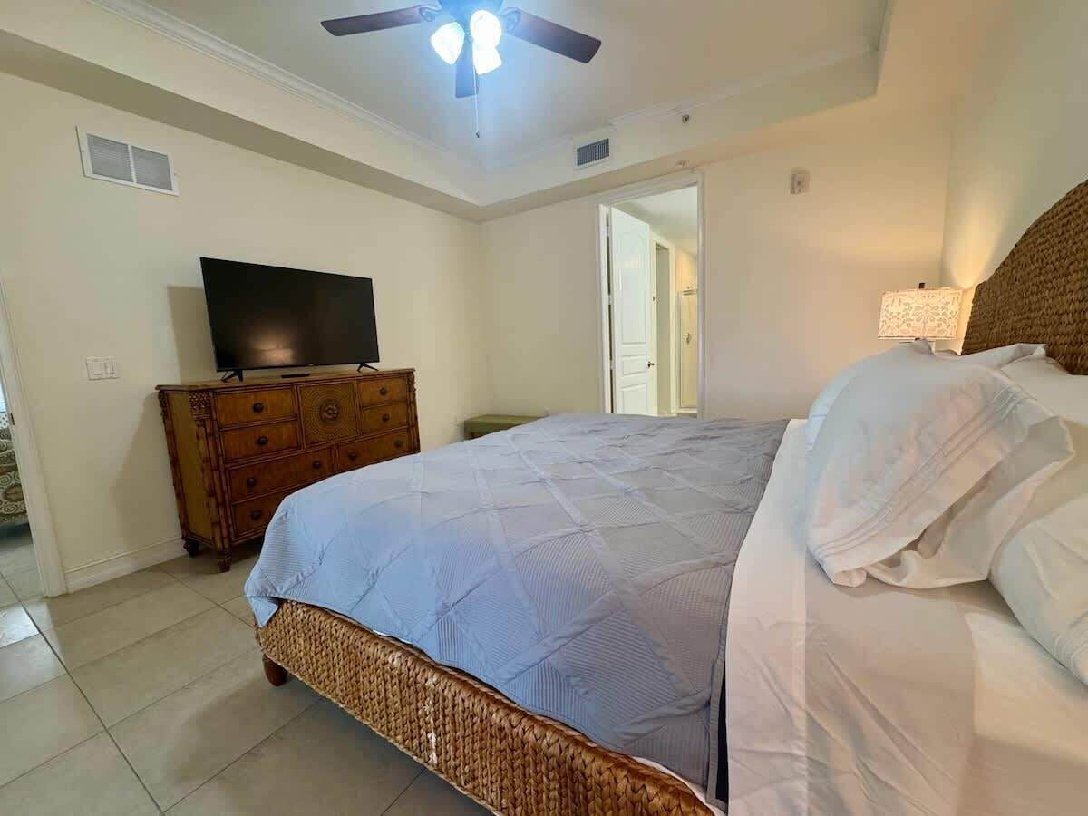 A bedroom with a bed, a dresser, a television, and a ceiling fan.